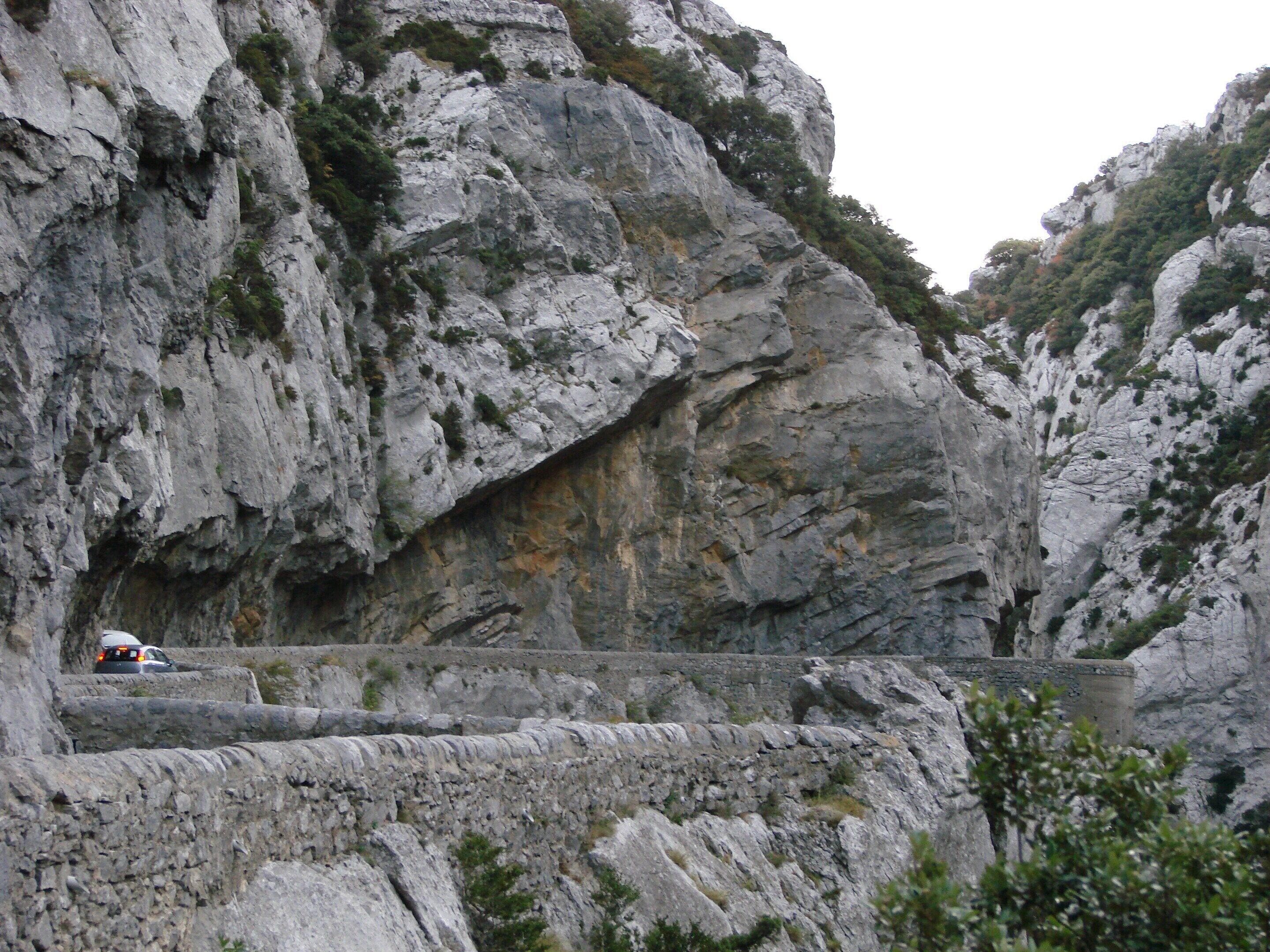 A rocky cliff with a narrow road and a stone bridge.