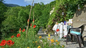Un jardín con mesa y sillas, rodeado de follaje y flores.