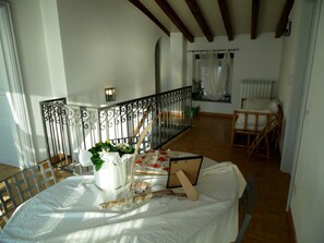 A room with a bed, a table with a vase and a book, a window with curtains, and a staircase.