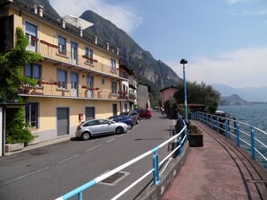 Une rue côtière bordée de voitures garées, avec un trottoir pour les piétons et des immeubles dotés de balcons donnant sur la mer.