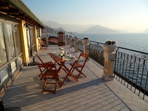 Une terrasse avec une table dressée pour le repas, des chaises, une balustrade et une vue sur la mer et les montagnes.