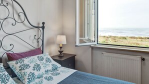 A bedroom with a bed, a nightstand, a lamp, a window with a view of the beach, and a radiator. - Holiday Home in Carrara by the Sea (Carrara)
