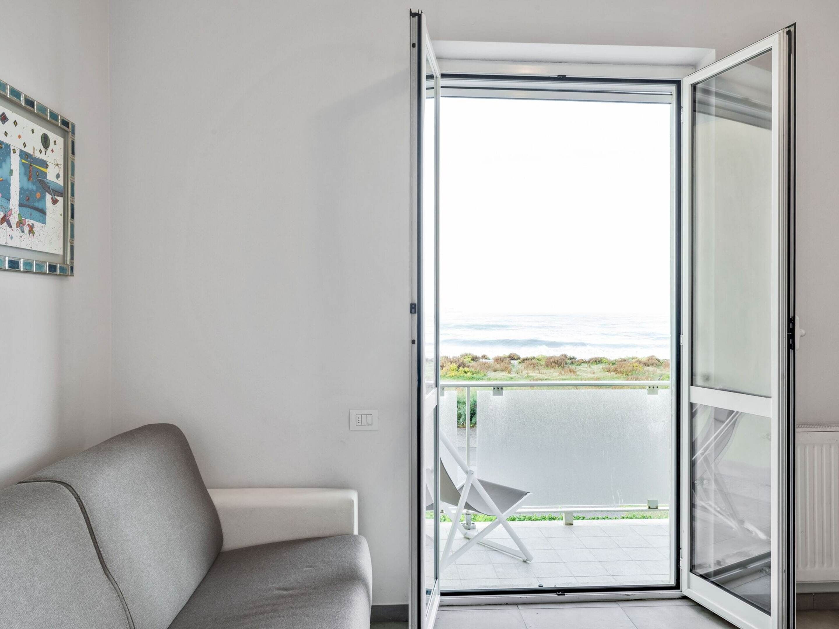 Una habitación con sofá gris, un radiador blanco y un balcón con una silla.