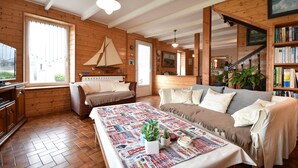 Ein gemütliches Zimmer mit Holzwänden, einer Couch, einem Tisch mit Zeitungen und einem Bücherregal.