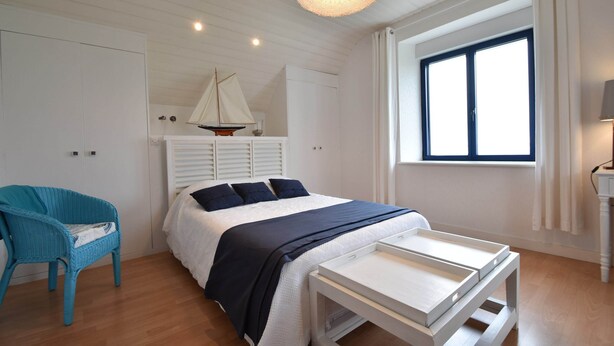 Ein Schlafzimmer mit einem Bett, einem kleinen Tisch, einem Stuhl, einem Fenster und einer Segelboot-Dekoration.