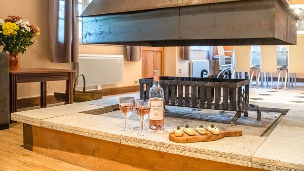 A bar area with a large metal grill, a bottle of rosé wine, two glasses, and a wooden board with snacks.