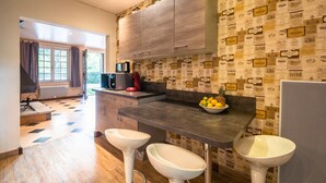 A kitchen with a wooden cabinet, a countertop, two white bar stools, a sink, and a window with curtains.