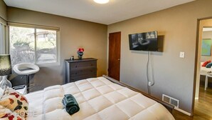 Un dormitorio con cama, escritorio, silla, cómoda, televisor y ventana.