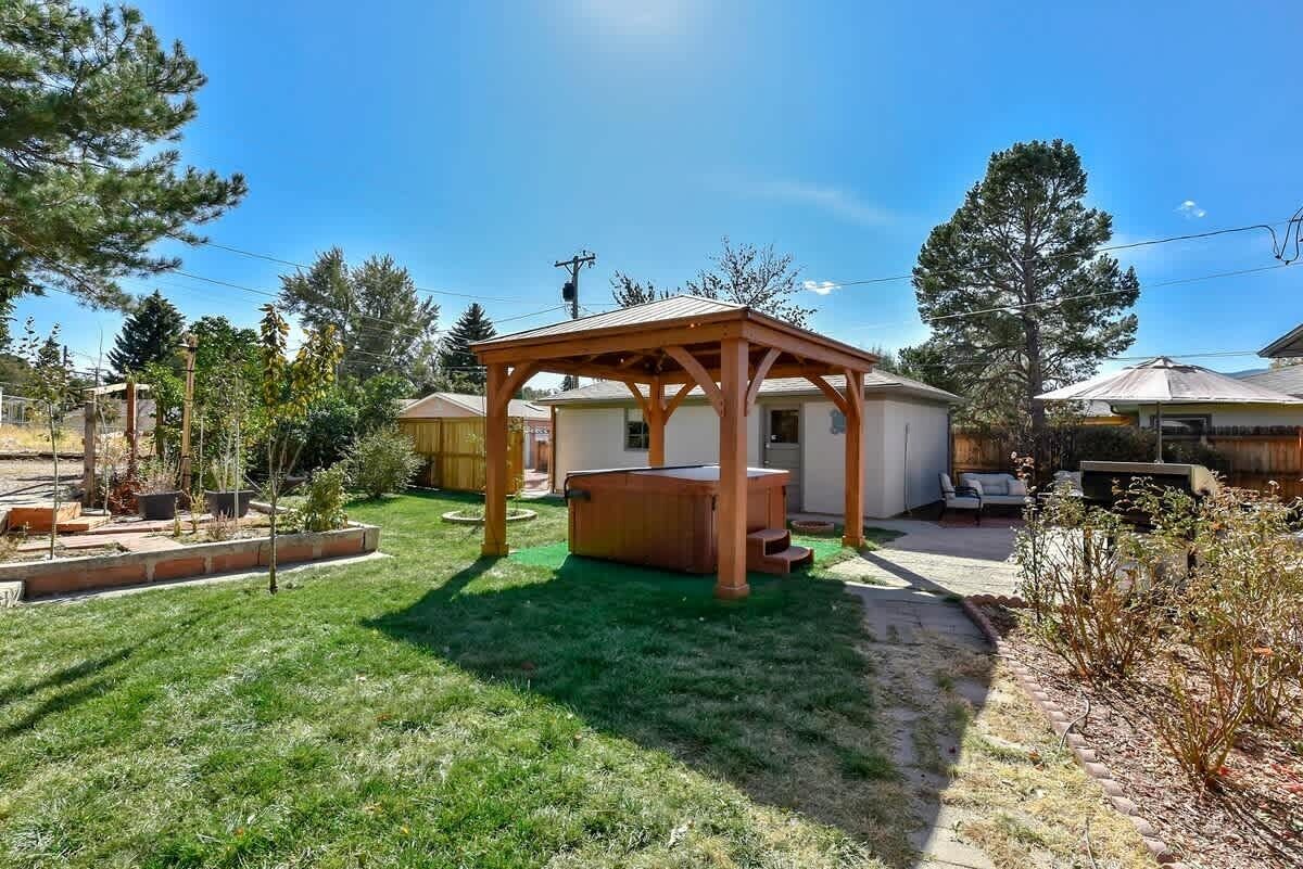 A backyard with a wooden pergola, a hot tub, and a lawn.