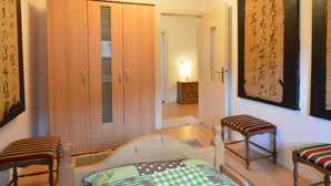 Un dormitorio con un armario de madera, una cama con colcha a cuadros, dos sillas a rayas y una obra de arte de caligrafía grande en la pared.