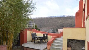 Un patio con una mesa y sillas, una pequeña escalera y vista a una colina boscosa.