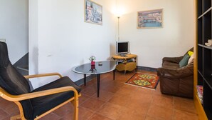 Un salon comprenant un canapé, un fauteuil, une petite table avec un téléviseur et deux tableaux accrochés au mur.