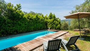 Une terrasse en bois avec une piscine, entourée d’un luxuriant feuillage verdoyant.