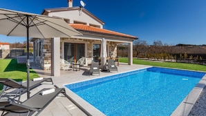A modern house with a swimming pool, outdoor furniture, and a stone facade.