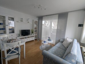 A modern living room with a sofa, TV, white cabinets, and a dining area. - Vintage Bungalow in Neubukow in Meeresnaehe (Neubukow)