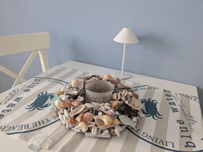A table with a striped tablecloth, a white lamp, and a centerpiece of various seashells. - Charmanter Bungalow in Neubukow Nahe der Ostsee (Neubukow)