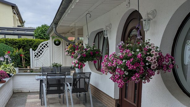 A patio with a table and chairs, a hanging flower basket, and a white fence. - Vintage Bungalow in Neubukow in Meeresnaehe (Neubukow)