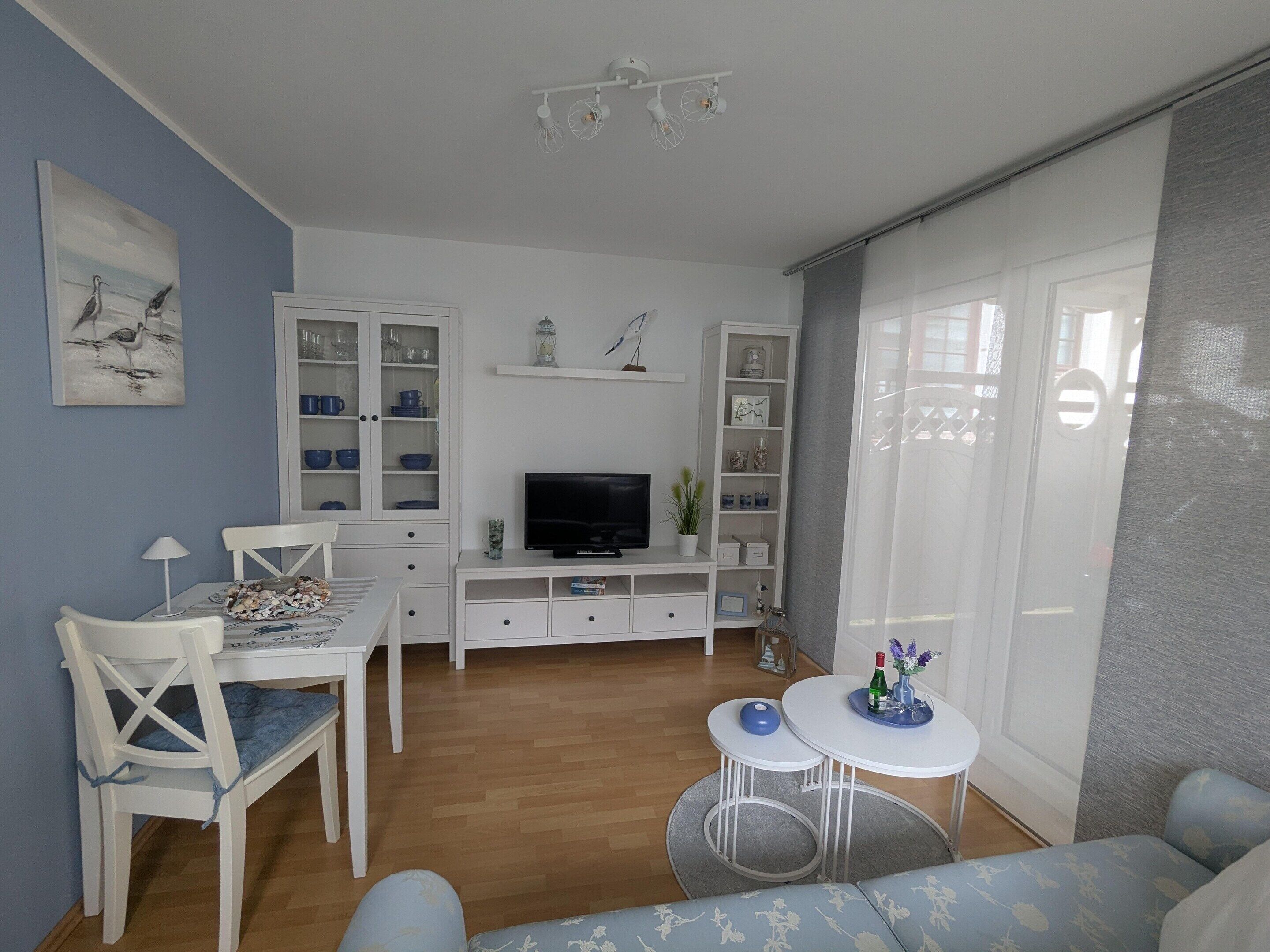 Un salon avec un téléviseur, des meubles blancs, une table à manger et un canapé.