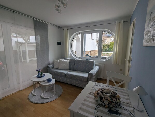Een moderne woonkamer met een bank, een klein rond tafeltje, een raam met gordijnen en uitzicht op buiten.