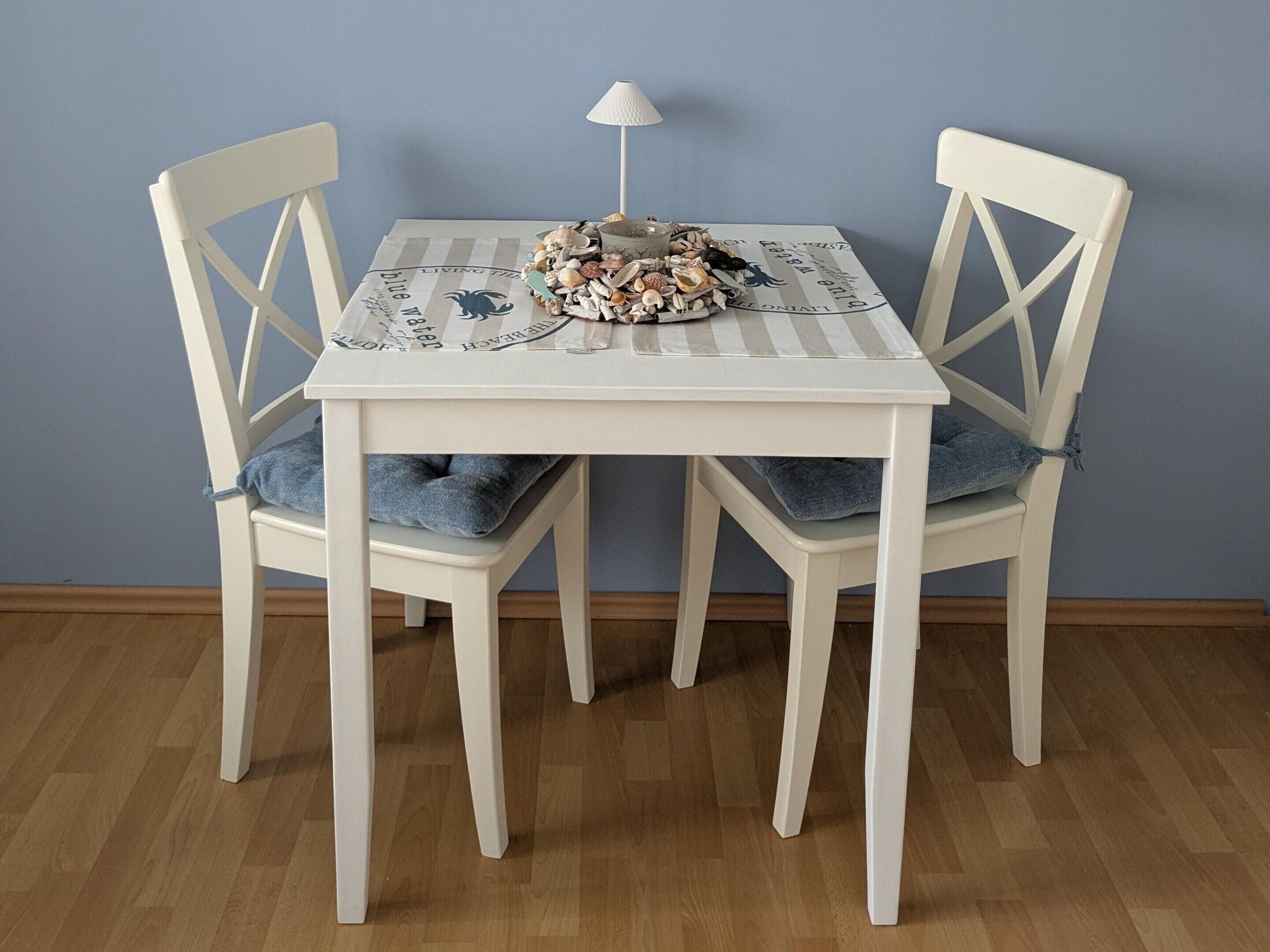A dining table with a placemat, two chairs with blue cushions, and a small lamp.
