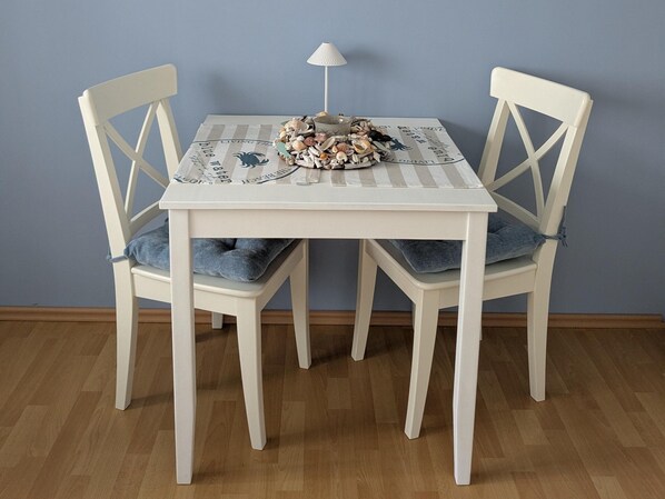 A dining table with a placemat, two chairs with blue cushions, and a small lamp. - Vintage Bungalow in Neubukow in Meeresnaehe (Neubukow)