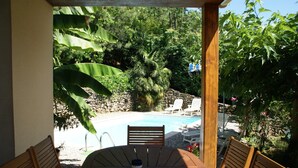 A wooden table with chairs, a pool, and lush greenery. - Family Escape in Les Salelles (Les Salelles)