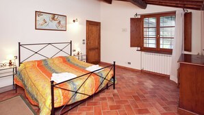 A bedroom with a bed, a wooden door, a window with shutters, a radiator, and a small table with a lamp. - Spacious Holiday Home (Bucine)