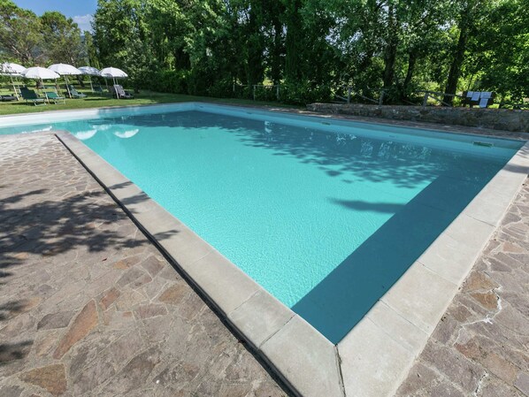 Guests can enjoy a refreshing swim in the pool surrounded by a lush lawn and trees.