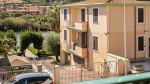 Un edificio a più piani con balconi, un vialetto recintato e una vista sul fiume e sulle colline sullo sfondo.