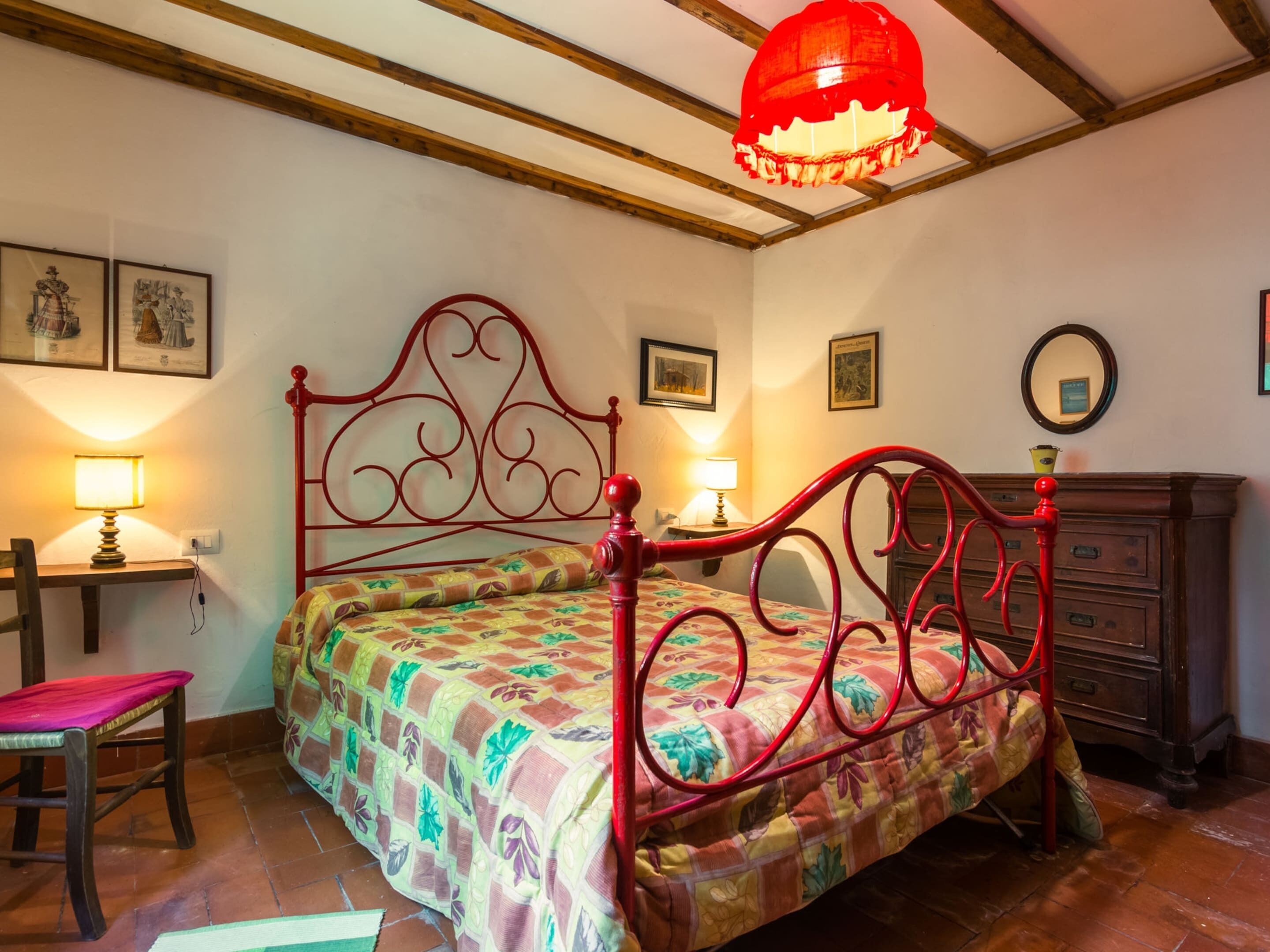 A bedroom with a wooden bed frame, two bedside lamps, a wooden dresser, and a red hanging light fixture.