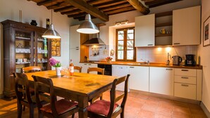 A rustic kitchen with wooden beams, a tiled floor, and a dining area with a wooden table and chairs.