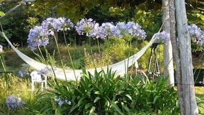 A garden with a hammock and purple flowers. - Woodland Escape With Pool (Vezzi Portio)