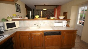 A kitchen with wooden cabinets, a microwave, a toaster, a sink, and a stone wall. - Cozy Family Home in Saint-pons (Saint-Pons)
