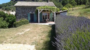 A stone house with a tiled roof, a small porch with chairs, and a lavender field adjacent to it. - Cozy Family Home in Saint-pons (Saint-Pons)