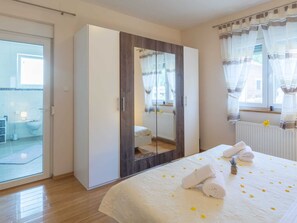 Une chambre dotée d’une grande armoire, d’un lit avec une couette blanche et des serviettes, d’une fenêtre avec des rideaux légers et d’une vue sur l’extérieur.