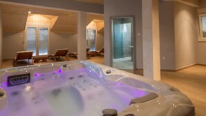 Ett modernt spa-rum med ett bubbelbad, träpanel i taket och en sittgrupp.