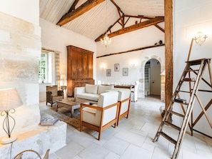 A rustic interior with exposed wooden beams, a white stone fireplace, and a dining area with a chandelier. - Holiday Home Saint-laurent Pool & Garden (Saint-Laurent-de-la-Salle)