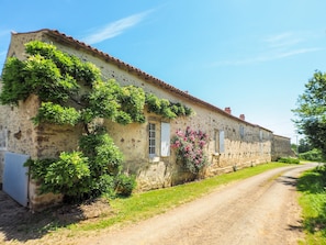 A rustic stone building with a dirt road in front, surrounded by greenery and flowering plants. - Holiday Home Saint-laurent Pool & Garden (Saint-Laurent-de-la-Salle)