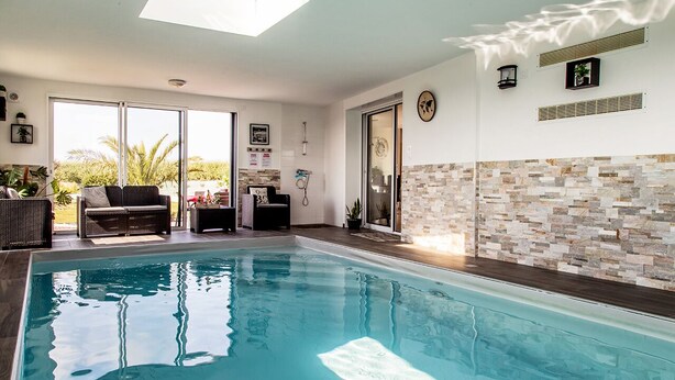 Una piscina con cerramiento de vidrio, un solárium con vistas y un muro de piedra.