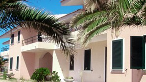 A two-story building with a balcony, a small garden, and a palm tree in the foreground. - Residence With Pool, Near the Beach and Coastal Town of La Ciacca (Valledoria)