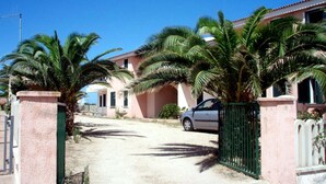 A residential area with houses, palm trees, and a parked car. - Residence With Pool, Near the Beach and Coastal Town of La Ciacca (Valledoria)