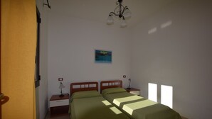 A bedroom with two beds, a nightstand with a lamp, a small table, and a wall-mounted picture. - Residence With Pool, Near the Beach and Coastal Town of La Ciacca (Valledoria)