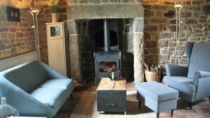 A stone fireplace with a modern wood-burning stove, two blue armchairs, a small wooden table, and a floor lamp. - Holiday Home in Ceauce Near Mont Saint Michel (Ceauce)