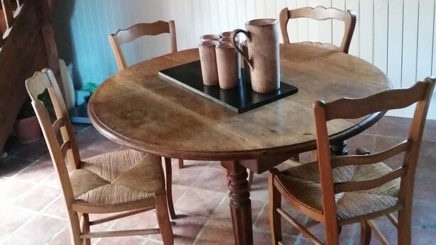 A round wooden table with chairs, a stone wall, and a staircase. - Holiday Home in Ceauce Near Mont Saint Michel (Ceauce)