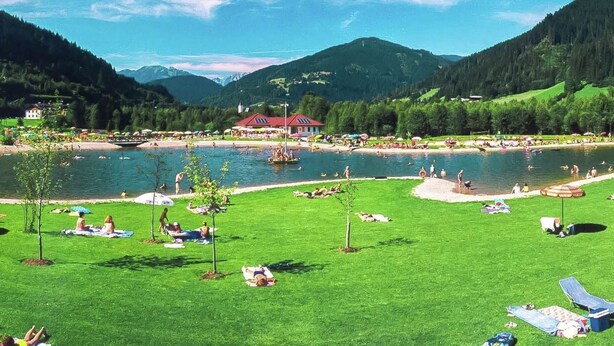 A lakeside resort with a red building, grassy areas, and a clear view of the mountains. - Mansion in Eben Near Ski Salzburger Sportwelt (Eben im Pongau)