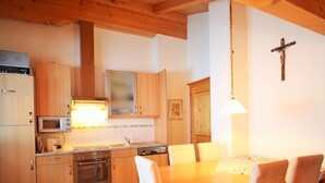 A kitchen with wooden cabinets, a microwave, stove, and a dining table with chairs. - Mansion in Eben Near Ski Salzburger Sportwelt (Eben im Pongau)