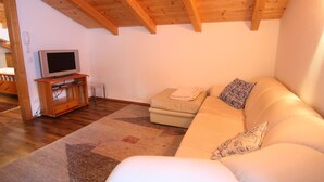 A living room with a wooden ceiling, a sofa, a TV on a wooden stand, and a patterned rug. - Mansion in Eben Near Ski Salzburger Sportwelt (Eben im Pongau)