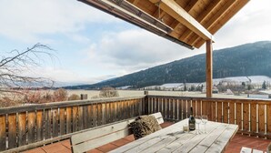 A wooden deck with a table and benches, overlooking a scenic landscape with hills and a distant village. - Chalet in ski Area in Mauterndorf With Sauna (Mauterndorf)