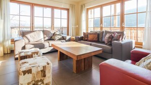 A spacious living room with large windows, a wooden coffee table, leather sofas, and a red armchair. - Chalet in ski Area in Mauterndorf With Sauna (Mauterndorf)