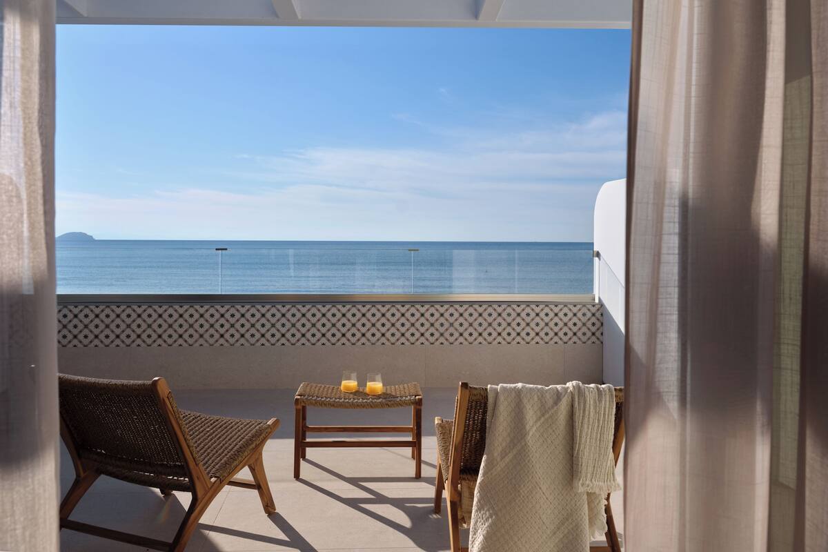 Un balcon avec des fauteuils en osier, une petite table avec des verres et une vue sur la mer.